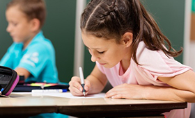 Schlerin, schreibend am Schultisch, und im Hintergrund ein Schler in einer Grundschule