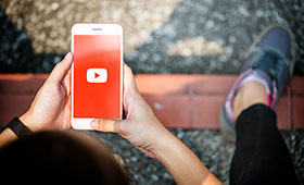 Jugendliche hlt ein Smartphone in der Hand, auf dem ein YouTube-Logo zu sehen ist