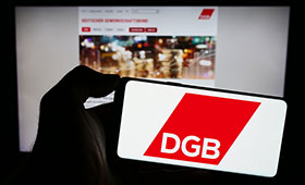 Eine Hand hlt ein Smartphone mit dem DGB-Logo vor dem Hintergrund der Website des DGB